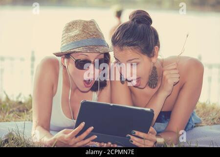 Closeup portrait two surprised girls looking at pad discussing latest gossip news. Young shocked funny women friends reading sharing social media news Stock Photo