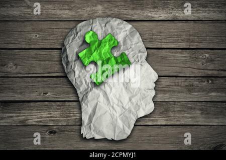 Puzzle head solution concept as a human face profile made from crumpled white paper with a jigsaw piece cut out inside the brain area on old wood back Stock Photo
