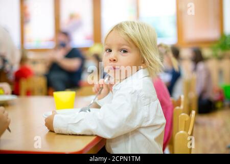 Blond toddler child, eating breakfast in kindergarden Stock Photo