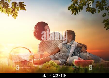 Family picnicking together. Young mother and her child daughter girl enjoying a healthy outdoor meal sitting together on green grass in summer park. Stock Photo