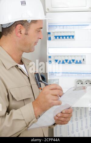 male technician holding clipboard while examining fusebox Stock Photo