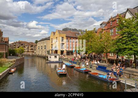 People enjoying a summer afternoon beside punts on the River Cam viewed from Magdalene Bridge, Cambridge, UK.