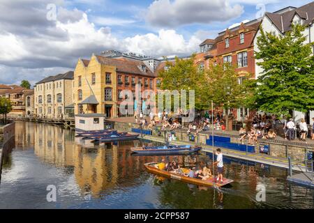People enjoying a summer afternoon beside punts on the River Cam viewed from Magdalene Bridge, Cambridge, UK.