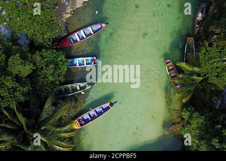 Aerial shot of White River, Ochos Rios, Jamaica with 4 colorful fishing boat moored in a small fishing settlement. Fishes are visible through the clea Stock Photo