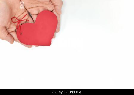 Top view of young male cupped hands holding a red heart shape tag in white background. Non-materialistic love is the best gift for birthday, christmas. Stock Photo