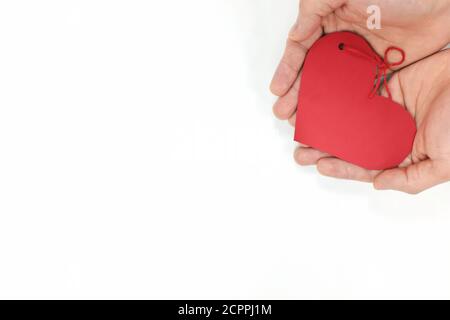 Top view of young male cupped hands holding a red heart shape tag in white background. Non-materialistic love is the best gift for birthday, christmas. Stock Photo