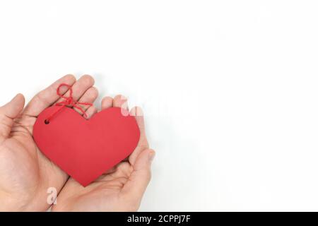 Top view of young male cupped hands holding a red heart shape tag in white background. Non-materialistic love is the best gift for birthday, christmas. Stock Photo