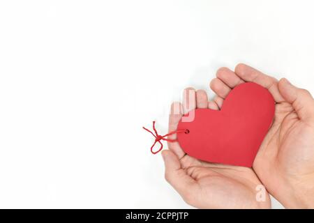 Top view of young male cupped hands holding a red heart shape tag in white background. Non-materialistic love is the best gift for birthday, christmas. Stock Photo