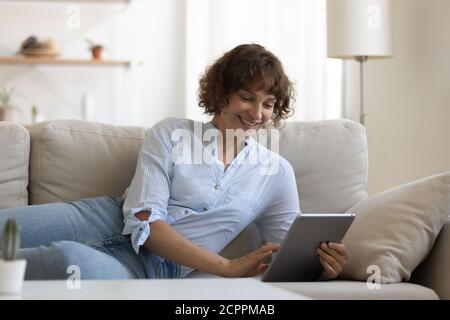 Smiling young woman relax on couch using tablet Stock Photo
