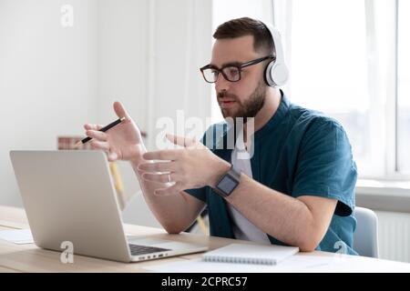 Serious businessman wearing headphones using laptop, speaking, making call Stock Photo