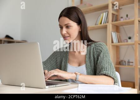 Smiling young businesswoman using laptop in office, looking at screen Stock Photo