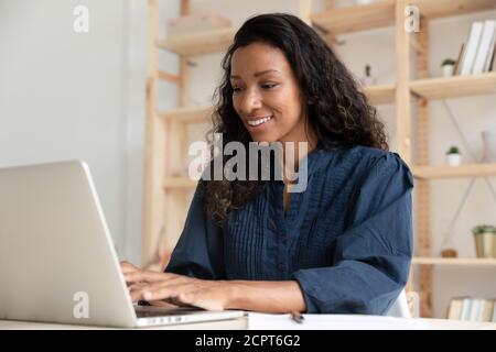 Smiling African American businesswoman using laptop, looking at screen Stock Photo
