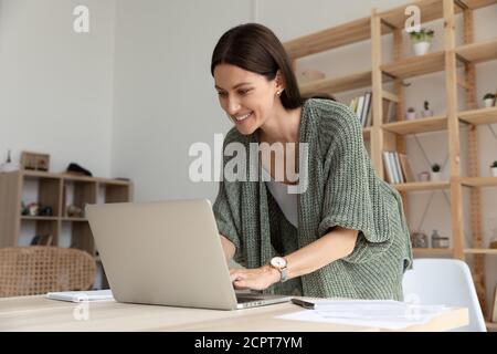 Interested smiling young businesswoman standing in office, working on laptop Stock Photo