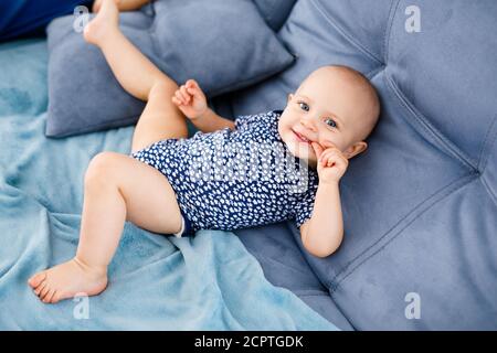 Portrait of happy laughing baby with blue eyes, in blue shirt, sitting on the couch Stock Photo