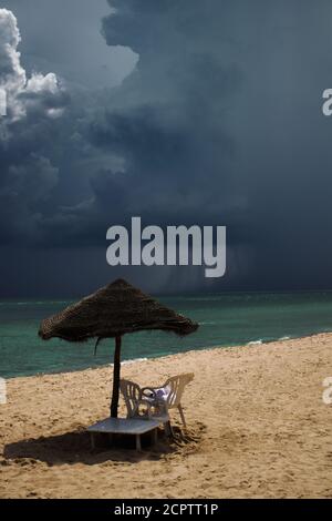 Mediterranean Sea with powerful storm in the background, light blue transparent water, sunbed with umbrella Stock Photo