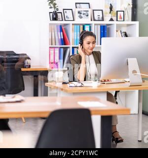 Young adult friendly confidence Asian woman with headsets working in a call center with social distance table as new normal practice. Call center and Stock Photo
