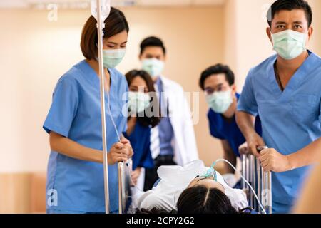 Seriously injured patient with oxygen mask on gurney stretcher bed pushed by medical team of doctor nurse and paramedic to the Operating Room. Emergen Stock Photo