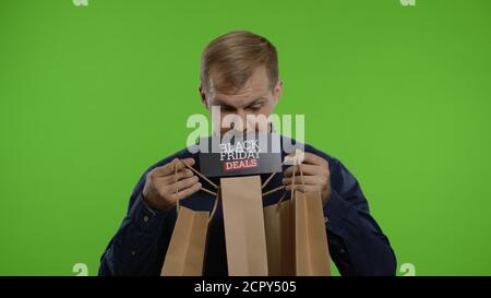 Surprised man showing shopping bags and Black Friday Deals inscription in his mouth. Good holiday sale discounts, low prices for shopping. Indoor on chroma key background. 6k downscale slow motion Stock Photo