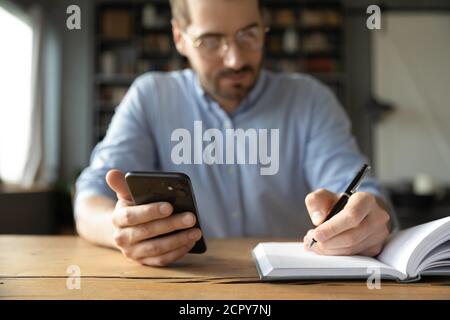 Close up of man use cellphone making notes in journal Stock Photo