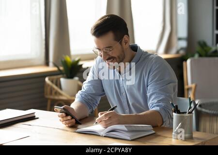 Smiling man use smartphone making notes planning Stock Photo