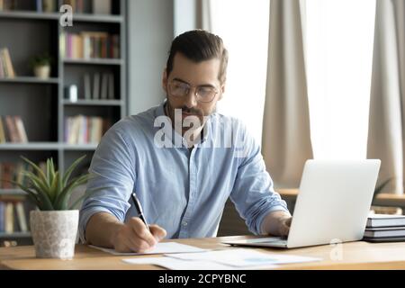 Young Caucasian man work on laptop making notes Stock Photo