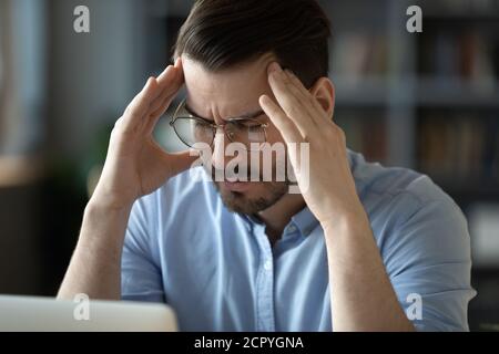Unwell young man suffering from headache at workplace Stock Photo