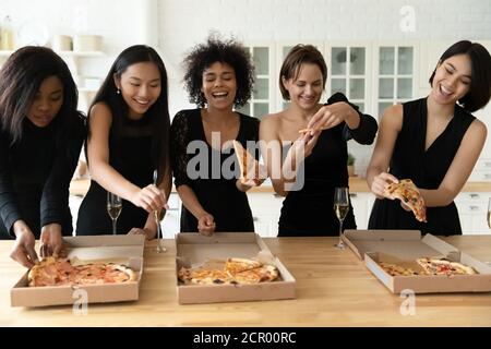 Happy young festive mixed race beautiful women eating pizza. Stock Photo