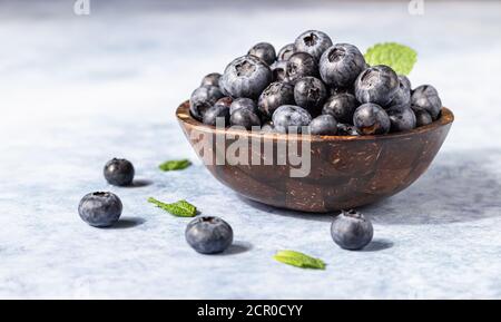 Freshly picked juicy blueberries in wooden bowl with mint on blue background. Antioxidant. Concept for healthy eating and nutrition. Bright light and Stock Photo