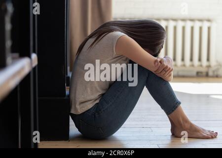 Distraught lady with arms around knees sitting alone on floor Stock Photo