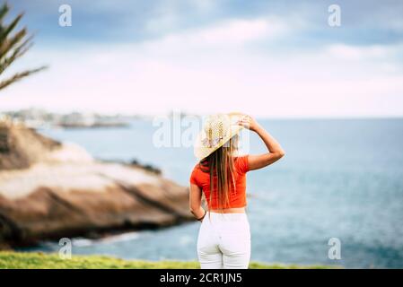 Tourism concept with beautiful female tourist viewed from back looking and enjoying the blue ocean and sky - summer holiday vacation and outdoor Stock Photo