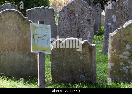Church graveyard headstones grouped closely together with a Coronavirus Social Distancing notice. Stock Photo