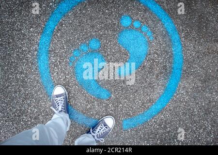 Man standing on blue dot. Sign painted on the pavement reminding users to maintain a physical distance of 3 feet / 1 meter during the COVID-19 pandemi Stock Photo