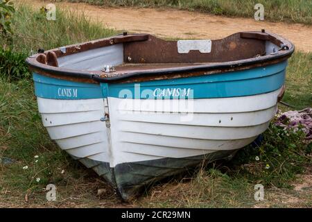 an old fashioned traditional clinker built wooden dinghy or boat high and dry on the seashore or beach. Stock Photo