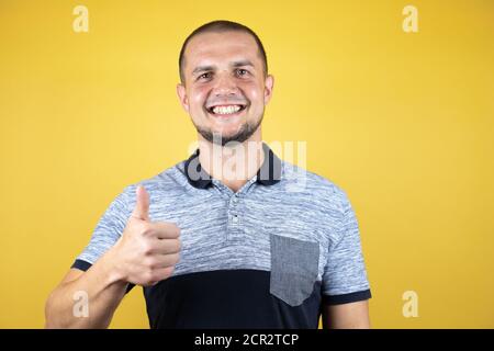 Russian man standing over insolated yellow background doing happy thumbs up gesture with hand. Approving expression looking at the camera with showing Stock Photo