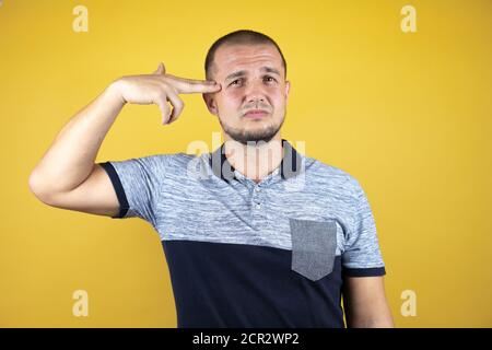 Russian man standing over insolated yellow background Shooting and killing oneself pointing hand and fingers to head like gun, suicide gesture. Stock Photo