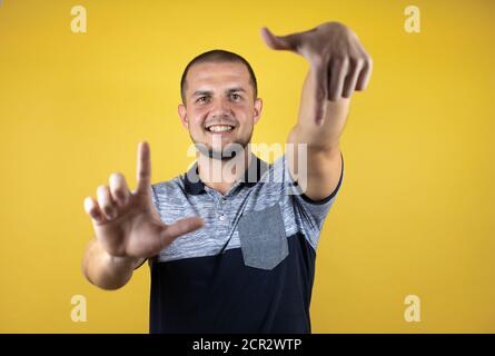 Russian man standing over insolated yellow background doing frame using hands palms and fingers, camera perspective Stock Photo