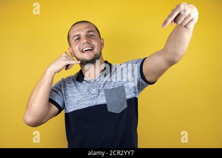 Russian man standing over insolated yellow background smiling doing phone gesture with hand and fingers like talking on the telephone and pointing the Stock Photo