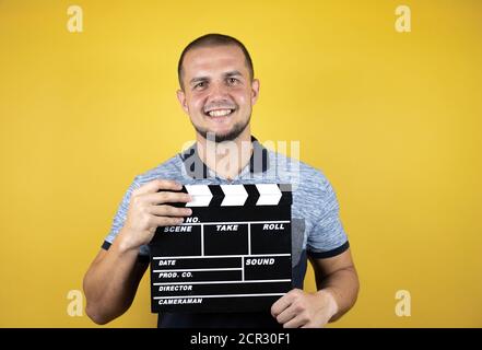Russian man standing over insolated yellow background standing over isolated yellow background holding clapperboard very happy Stock Photo