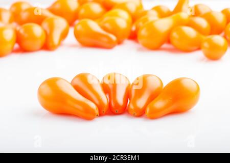 Five small ripe orange grape tomatoes and bunch of tomatoes on the back, isolated on white background. side view, close up. Stock Photo