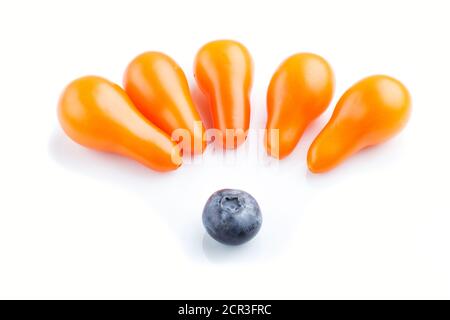 Five small ripe orange grape tomatoes and a single blueberry isolated on white background. top view, close up. contrast and diversity concept. Stock Photo