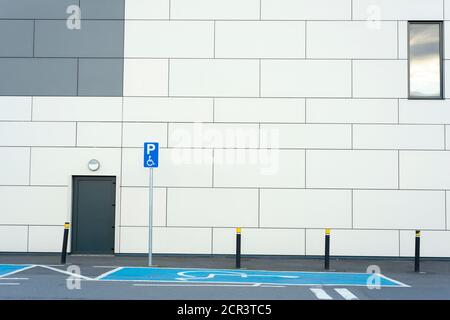 Empty disabled handicap parking space bay with blue marking and handicapped sign symbol by building wall. Stock Photo