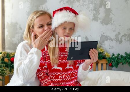 Christmas online family congratulations. Smiling european blonde mother and daughter using mobile tablet for video call friends and parents Stock Photo