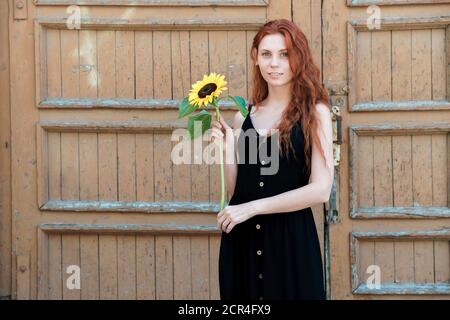 Girl with sunflower in hand on background of old wooden door. Simplicity and sincerity concept. Stock Photo