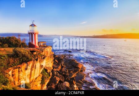 Warm rising sun light on HOrnby lighthouse and sandstone cliffs at entrance to Sydney harbour. Stock Photo