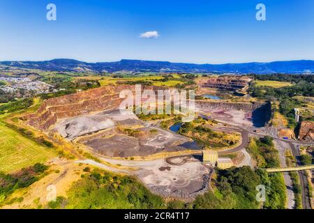 Scale of Bombo quarry granite mineral open pit mine and excavation in aerial view of a sunny day. Stock Photo