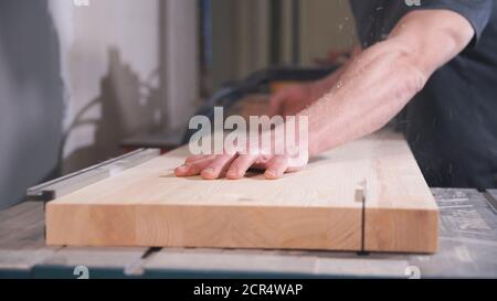 Woodworker works on machine with wooden board. Carpenter saws wood on circular saw machine. Stock Photo
