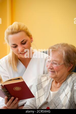 Generations in dialogue. In the day clinic of a geriatric unit, a patient is cared for during everyday exercises by a young woman doing voluntary Stock Photo