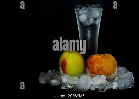 photo glass with ice thawing frozen apples among ice cubes close-up on a black background Stock Photo