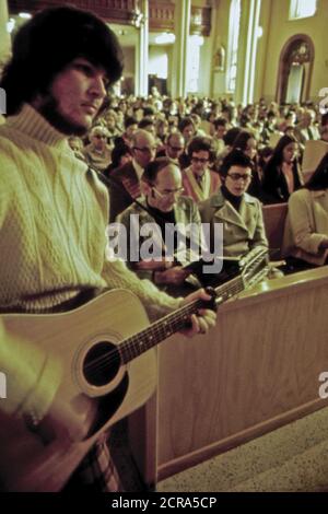 A Member of the New Ulm Cathedral Parish Is Shown Playing a Guitar at a Folk Mass. This Weekly Event Was Begun for the Young People and Has Become the Most Popular Mass with Standing Room Only. The Church Interior Is Decorated with Baroque Carvings Reminiscent of Churches in Southern Germany's Bavarian ca.1975 Stock Photo