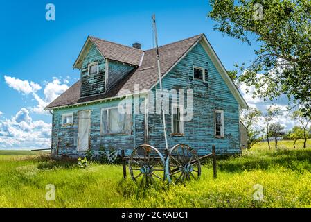 Old, abandoned blue prairie farmhouse with trees, grass and blue sky in Kayville, Saskatchewan, Canada Stock Photo